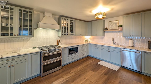 kitchen featuring decorative backsplash, appliances with stainless steel finishes, premium range hood, dark wood-type flooring, and sink