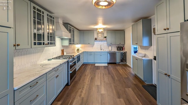 kitchen featuring appliances with stainless steel finishes, tasteful backsplash, premium range hood, sink, and dark hardwood / wood-style floors