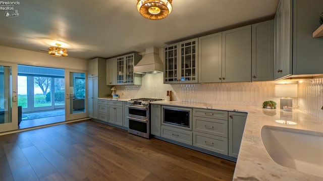 kitchen with premium range hood, light stone counters, built in microwave, double oven range, and dark hardwood / wood-style floors