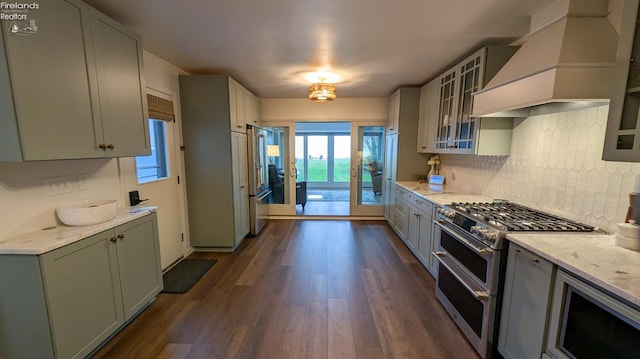 kitchen featuring light stone countertops, dark wood-type flooring, decorative backsplash, custom range hood, and appliances with stainless steel finishes