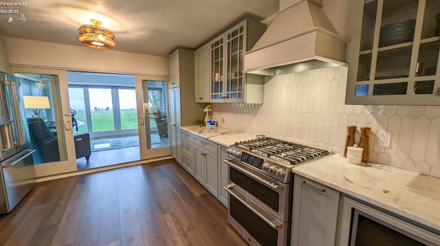 kitchen featuring backsplash, premium range hood, appliances with stainless steel finishes, dark hardwood / wood-style flooring, and light stone counters