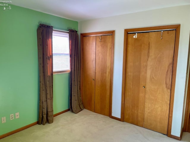 unfurnished bedroom featuring light carpet and two closets