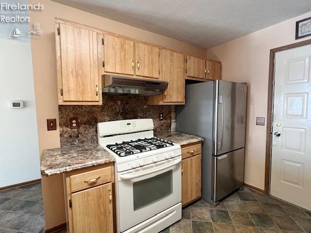 kitchen featuring light brown cabinetry, tasteful backsplash, a textured ceiling, white range with gas stovetop, and stainless steel refrigerator