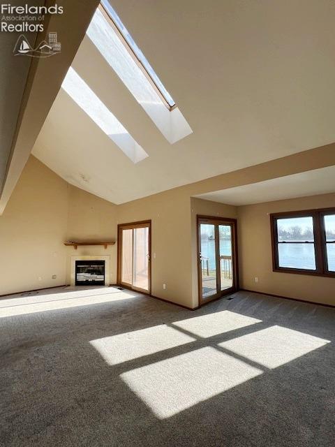 unfurnished living room featuring carpet, a skylight, and high vaulted ceiling