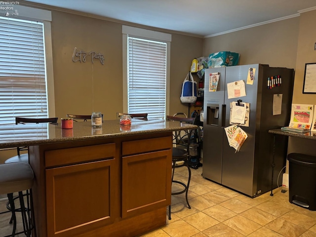 kitchen with dark stone countertops, stainless steel fridge, crown molding, and a healthy amount of sunlight