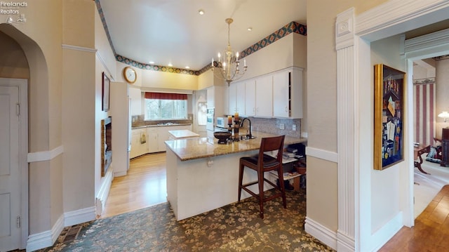 kitchen featuring a breakfast bar, stone counters, white cabinets, decorative backsplash, and kitchen peninsula