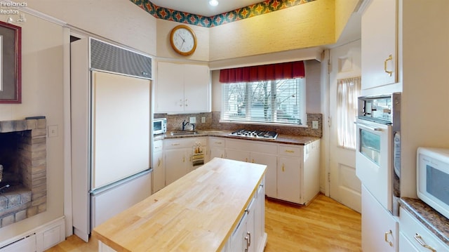 kitchen with white cabinetry, wooden counters, light hardwood / wood-style floors, white appliances, and a fireplace