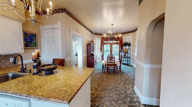 kitchen with pendant lighting, white cabinets, sink, stainless steel dishwasher, and light stone counters