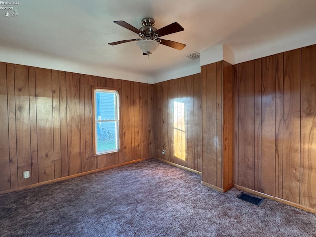 spare room with dark colored carpet, ceiling fan, and wooden walls