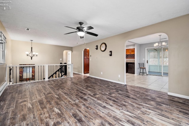 unfurnished room with ceiling fan with notable chandelier and light hardwood / wood-style flooring