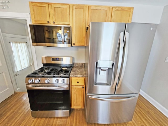 kitchen featuring appliances with stainless steel finishes, light wood-type flooring, dark stone counters, and light brown cabinetry