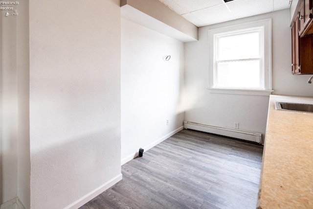 unfurnished dining area with a paneled ceiling, sink, wood-type flooring, and baseboard heating