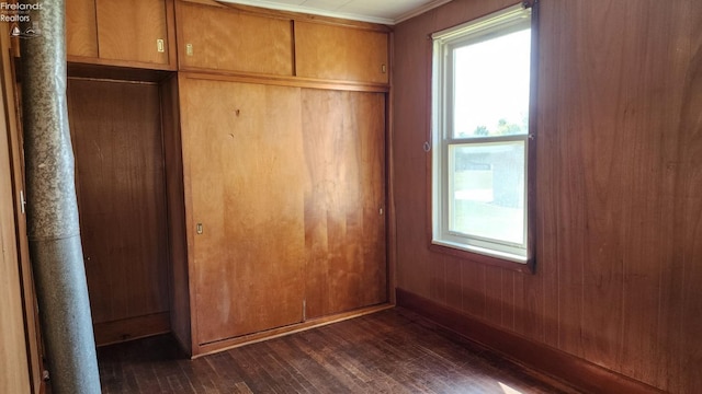 unfurnished bedroom featuring crown molding, dark wood-type flooring, wooden walls, and a closet