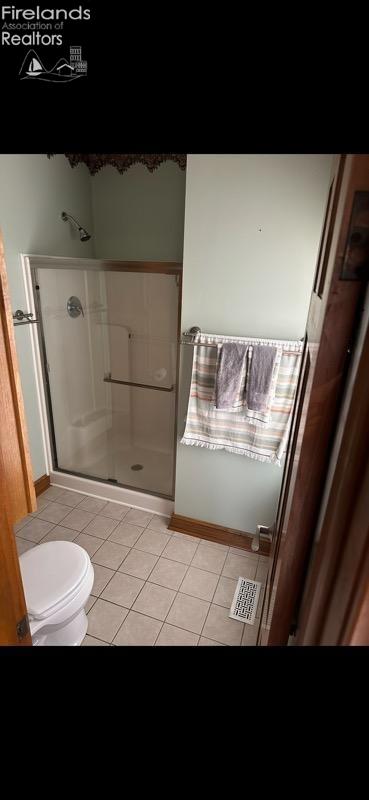 bathroom with tile patterned floors, toilet, and a shower with shower door