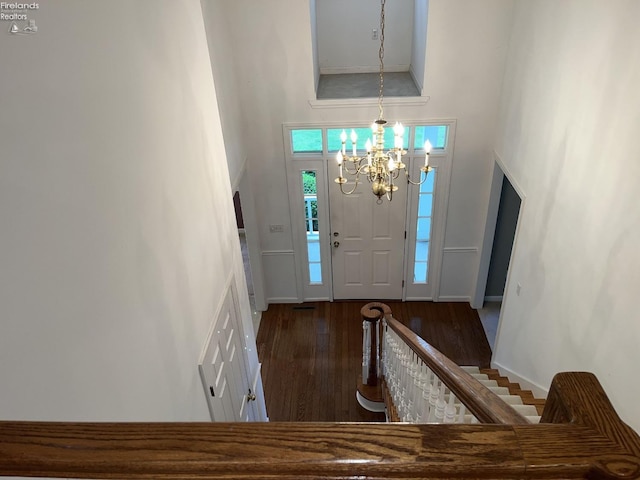 entrance foyer with a chandelier, a towering ceiling, and dark wood-type flooring