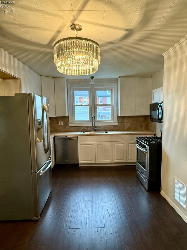 kitchen featuring sink, stainless steel appliances, an inviting chandelier, pendant lighting, and decorative backsplash