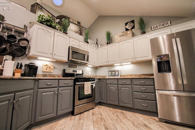 kitchen featuring light wood-type flooring, stainless steel appliances, vaulted ceiling, gray cabinets, and white cabinetry