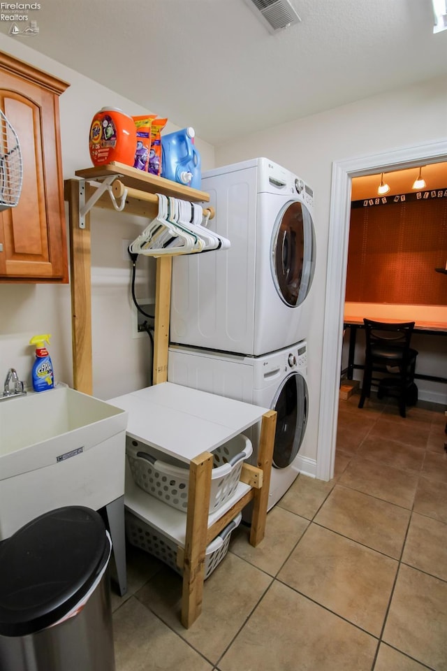 washroom featuring sink, light tile patterned floors, cabinets, and stacked washer / drying machine