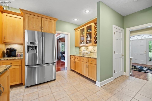 kitchen with stainless steel refrigerator with ice dispenser, backsplash, light stone counters, and light tile patterned floors