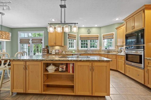 kitchen featuring black appliances, a center island, pendant lighting, and light stone counters