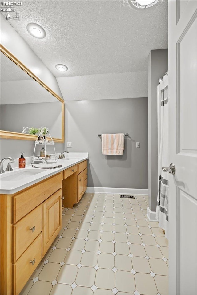 bathroom featuring a textured ceiling, vanity, and lofted ceiling