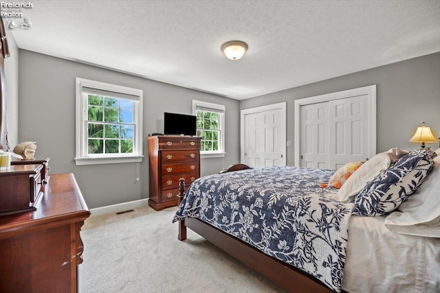 bedroom with two closets, a textured ceiling, and light colored carpet