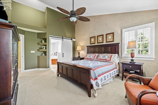 carpeted bedroom featuring ceiling fan, a barn door, high vaulted ceiling, and ensuite bath