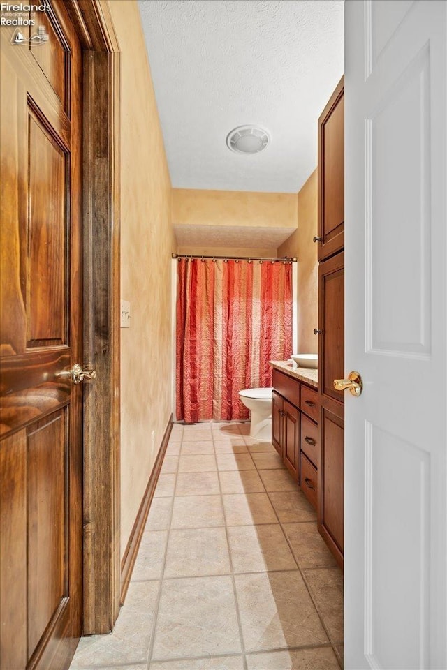 bathroom featuring tile patterned floors, vanity, toilet, and a textured ceiling