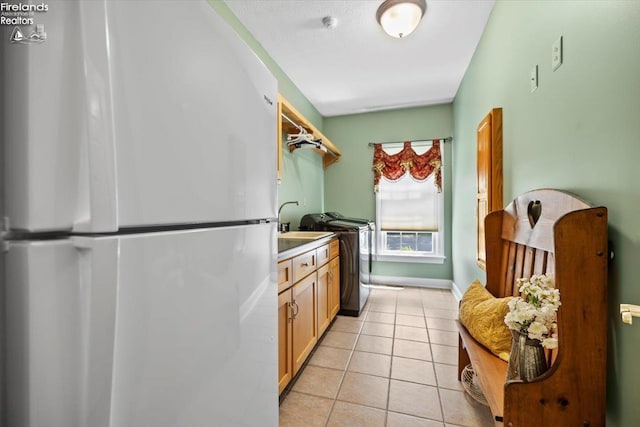 kitchen featuring stainless steel fridge, washer / dryer, light tile patterned floors, and light brown cabinetry