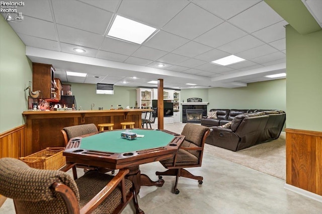 playroom featuring a drop ceiling, light carpet, a tile fireplace, wooden walls, and indoor bar