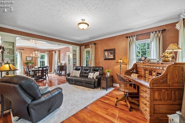 living room featuring an inviting chandelier, ornamental molding, decorative columns, a textured ceiling, and hardwood / wood-style flooring