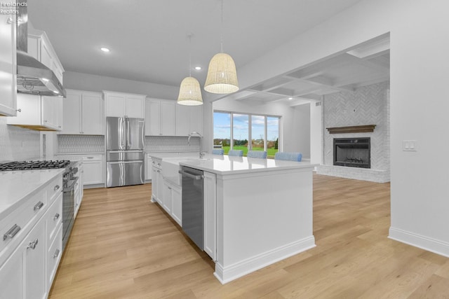 kitchen with a fireplace, appliances with stainless steel finishes, white cabinetry, and an island with sink