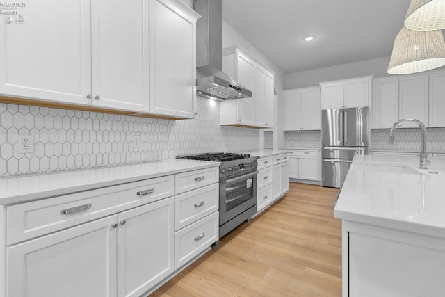 kitchen with appliances with stainless steel finishes, wall chimney exhaust hood, sink, decorative light fixtures, and white cabinetry