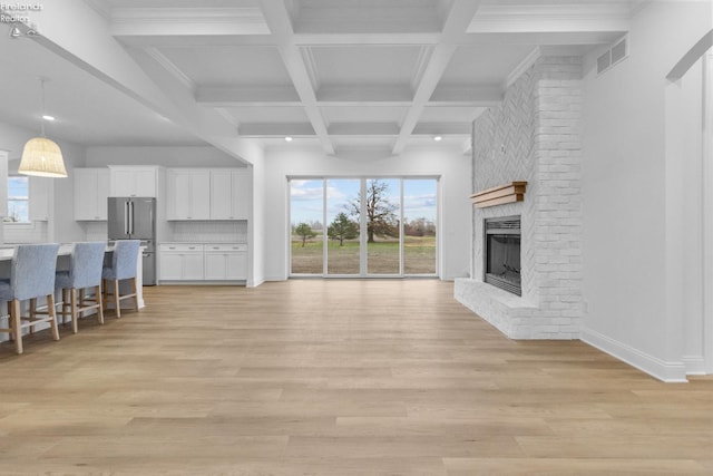 unfurnished living room with coffered ceiling, beam ceiling, light wood-type flooring, and a brick fireplace