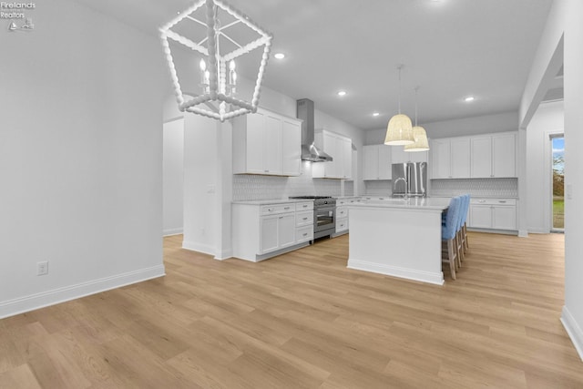 kitchen featuring white cabinets, appliances with stainless steel finishes, a kitchen island with sink, and wall chimney range hood