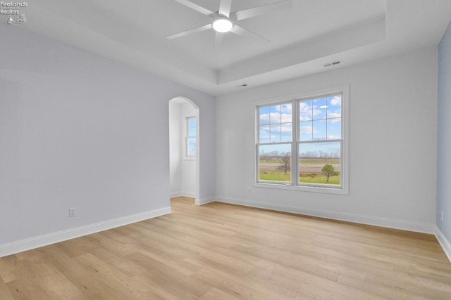 unfurnished room featuring a tray ceiling, ceiling fan, and light hardwood / wood-style floors