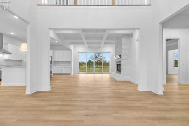 unfurnished living room featuring beamed ceiling, light hardwood / wood-style floors, a fireplace, and coffered ceiling