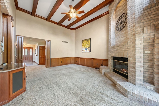 carpeted living room featuring beam ceiling, a brick fireplace, ceiling fan, and a high ceiling