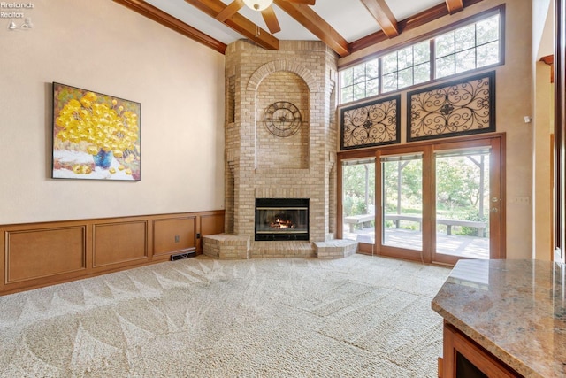 carpeted living room featuring beam ceiling, ceiling fan, a high ceiling, and a brick fireplace