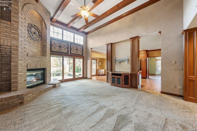 unfurnished living room with light carpet, a towering ceiling, a brick fireplace, ceiling fan, and beam ceiling