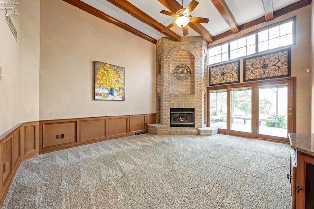 unfurnished living room featuring ceiling fan, a towering ceiling, a fireplace, beam ceiling, and carpet floors