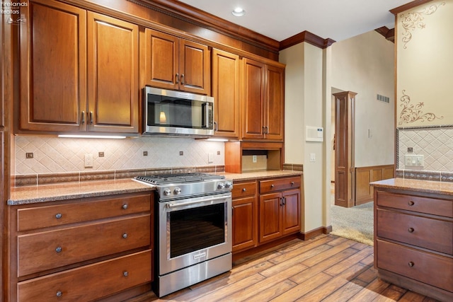 kitchen featuring crown molding, light stone counters, stainless steel appliances, and light hardwood / wood-style flooring