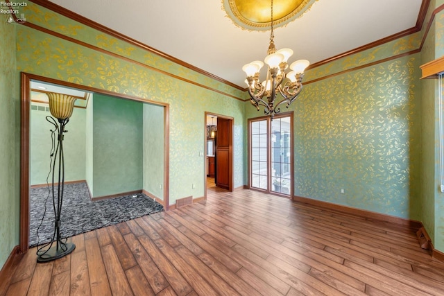 spare room with hardwood / wood-style flooring, crown molding, and a chandelier