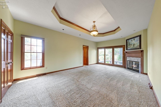 unfurnished living room featuring light carpet, a tray ceiling, plenty of natural light, and a high end fireplace