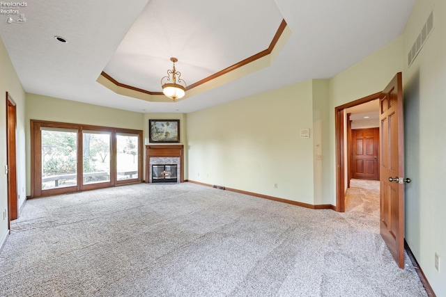 unfurnished living room featuring a raised ceiling, light colored carpet, and a fireplace