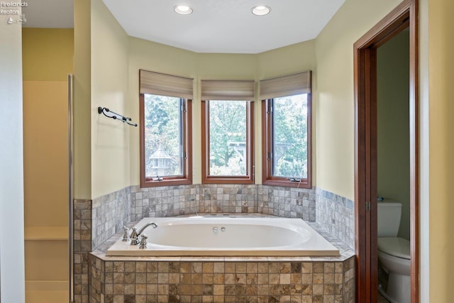 bathroom with tiled bath, plenty of natural light, and toilet