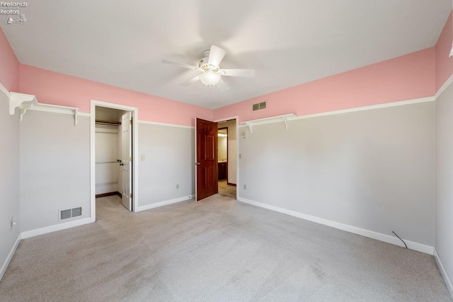 unfurnished bedroom featuring light carpet, a closet, a spacious closet, and ceiling fan