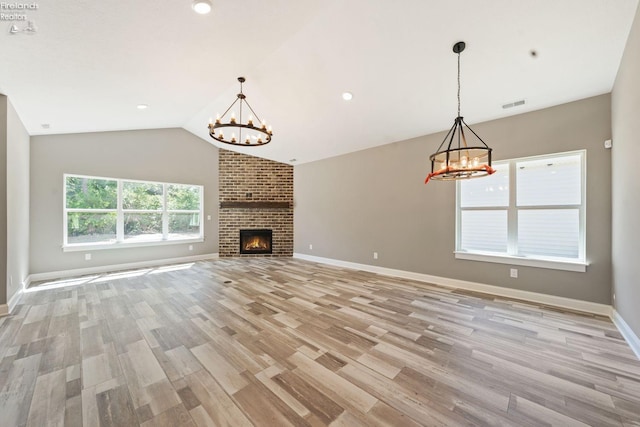 unfurnished living room with visible vents, lofted ceiling, light wood-style flooring, an inviting chandelier, and a brick fireplace