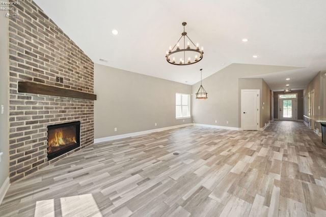 unfurnished living room featuring baseboards, lofted ceiling, light wood-style flooring, a fireplace, and a notable chandelier