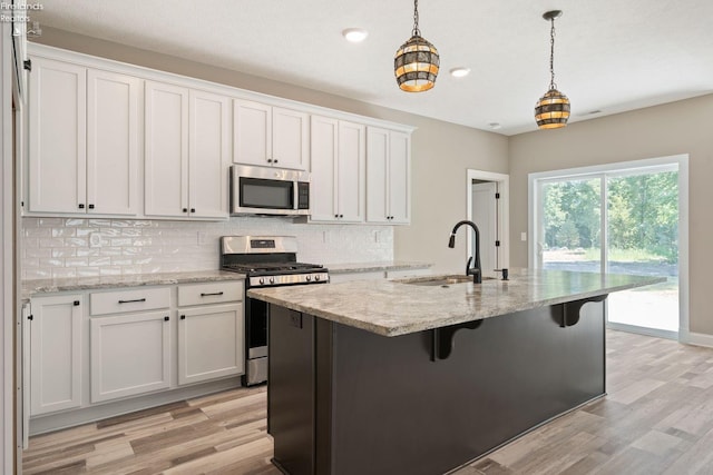 kitchen featuring tasteful backsplash, white cabinets, hanging light fixtures, stainless steel appliances, and a sink